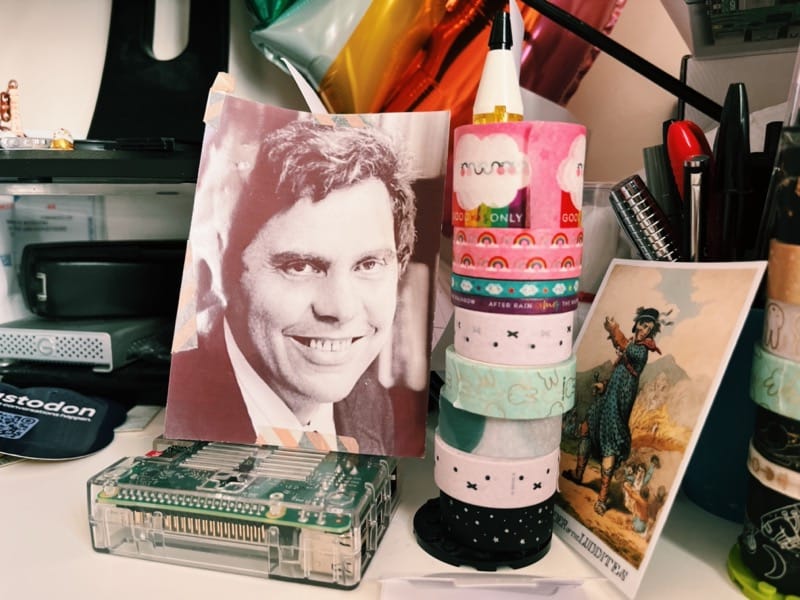 a photo of my messy desk: a black and white picture of the late Neil Postman is sitting on top of my Raspberry Pi 3