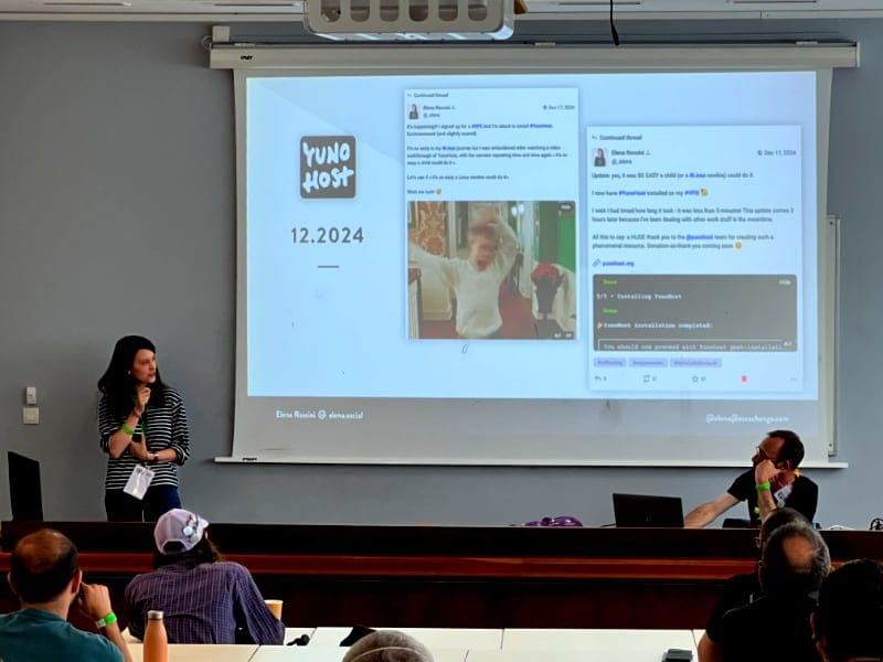 a photo showing a woman in front of a classroom with a large screen behind her that shows a slide from her presentation. On it there is the YunoHost logo and two screenshots of Mastodon toots about her YunoHost installation