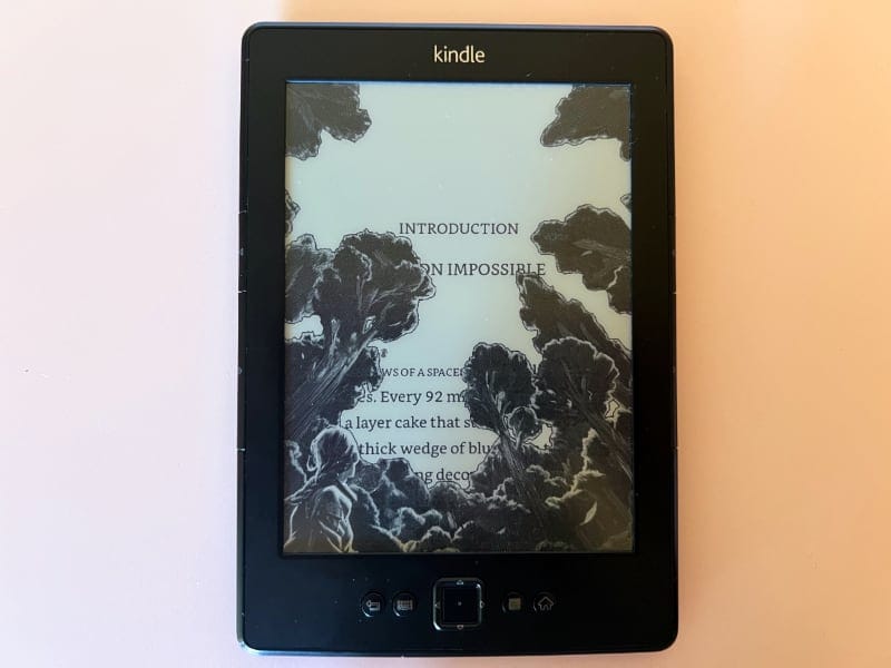 an overhead photo of my Kindle in sleep mode showing the "Katniss" screensaver - as in: Katniss Everdeen from the Hunger Games. Through the screensaver you can see words from the page of a Kindle